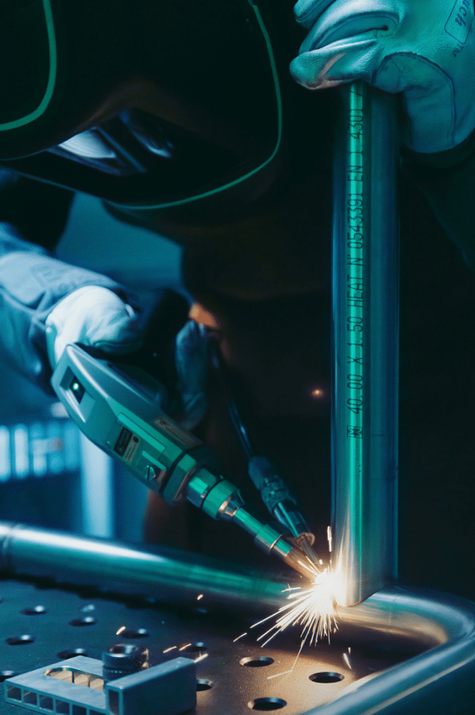 Uomo con tutti i dispositivi di protezione individuale per la saldatura laser che usa una saldatrice laser su una ringhiera.